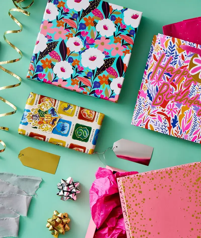 Colourful wrapped gifts, a floral pattern box, greeting cards, gift bags, ribbons and bows arranged on a mint green background.